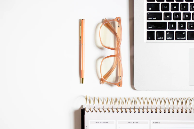 Escritorio blanco con portátil, gafas, bolígrafo dorado y planificador
