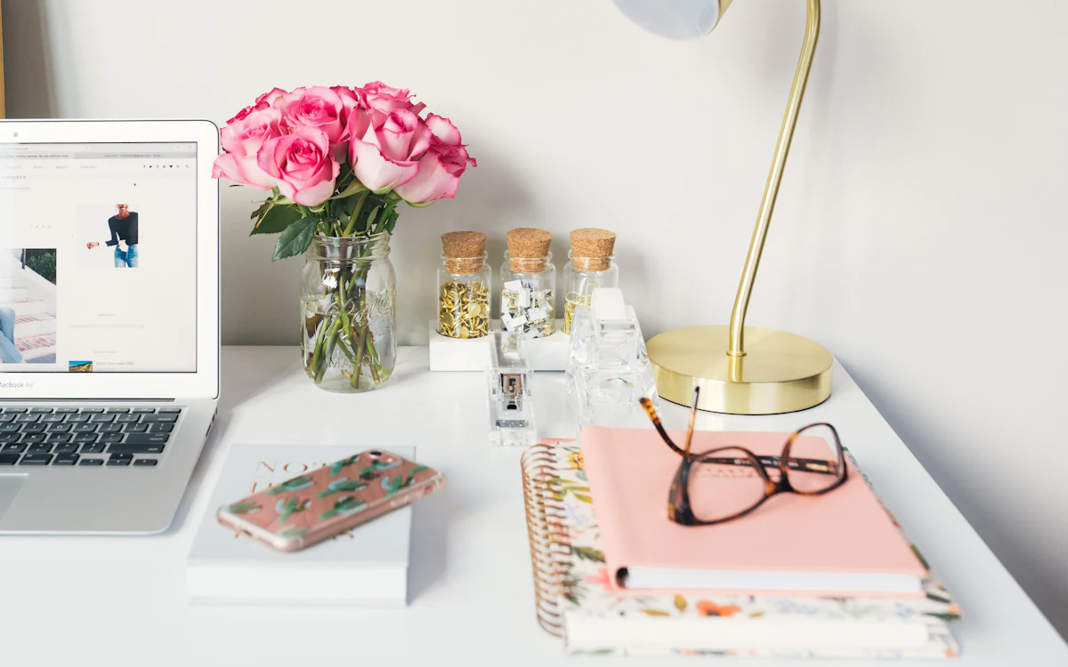 Escritorio con portátil, lámpara dorada, flores rosas y agendas
