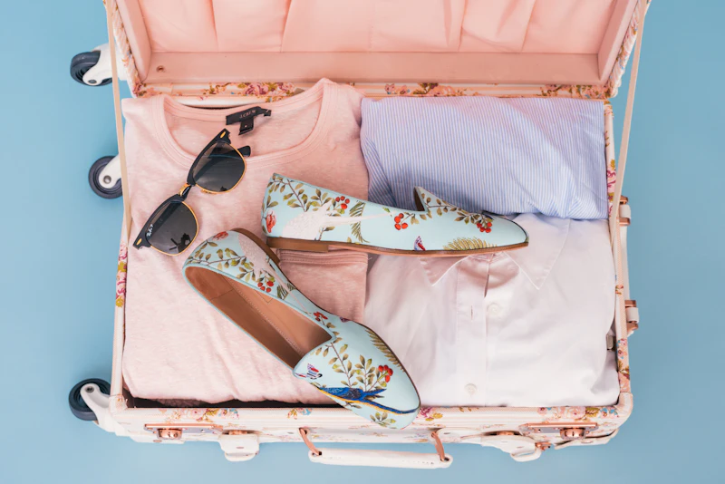 Maleta abierta con ropa doblada, gafas de sol y zapatos estampados